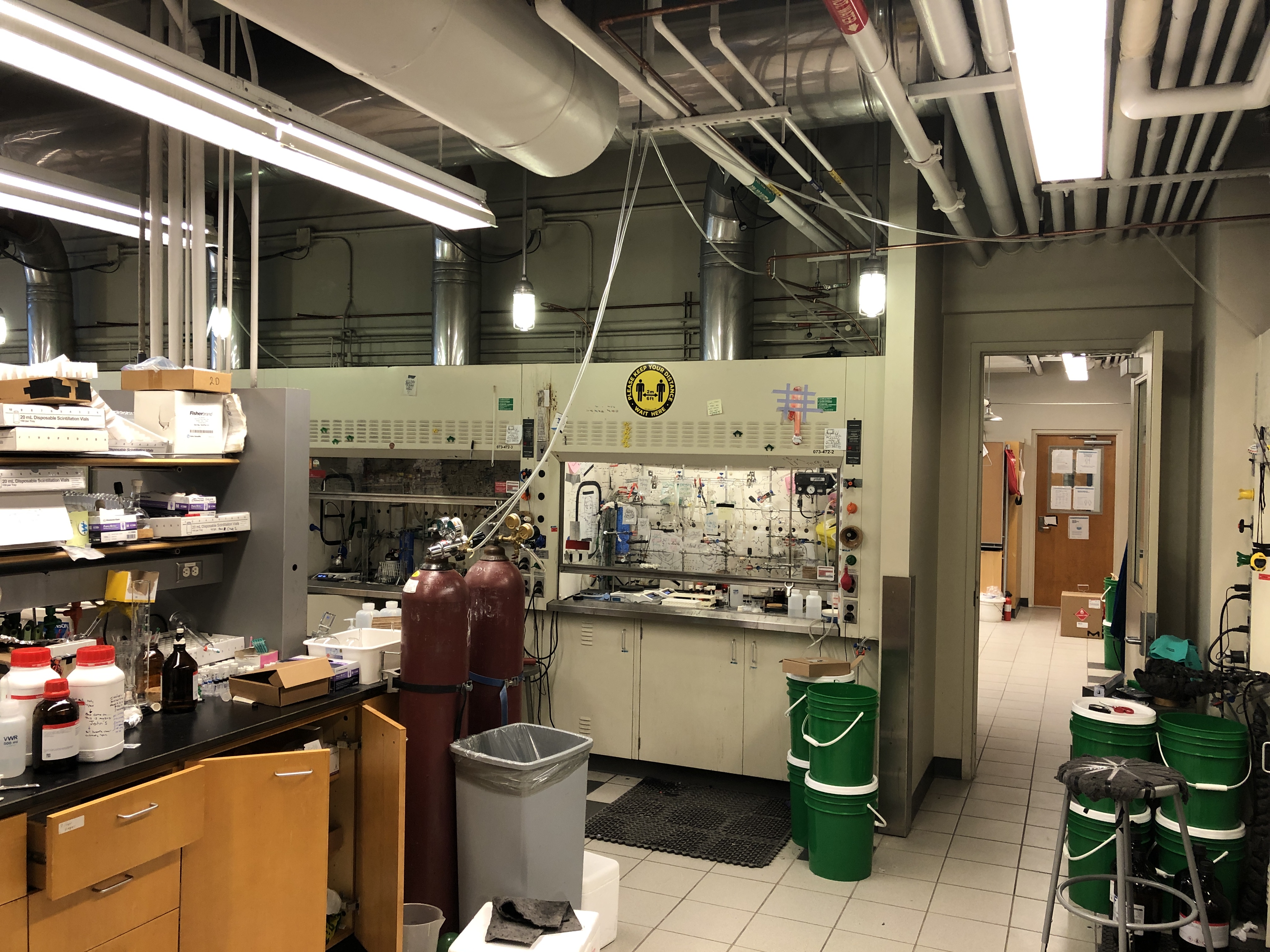 Shot of lab space in room 472 showing research bench on the left, fumehoods in the middle, and door connecting to lab 473 on the right side.