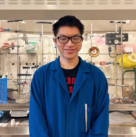 Terry in a blue lab coat standing in front of a lab fume hood.