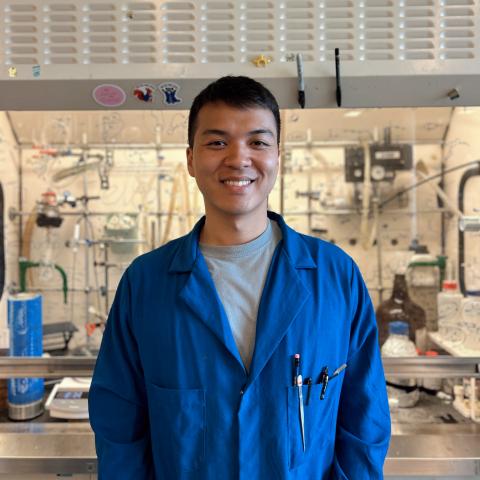 Brian in a blue lab coat standing in front of a lab fume hood.
