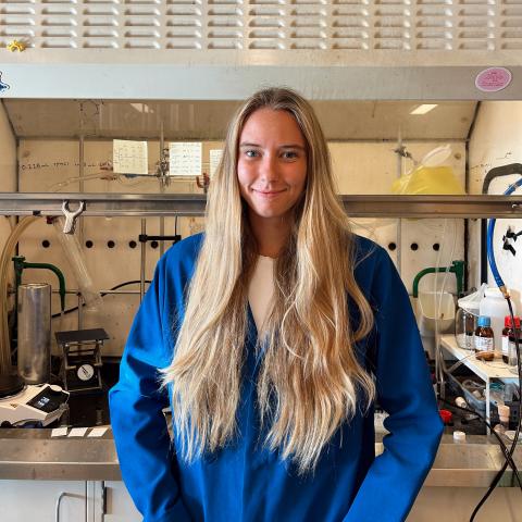 Bridget in a blue lab coat standing in front of a lab fume hood.